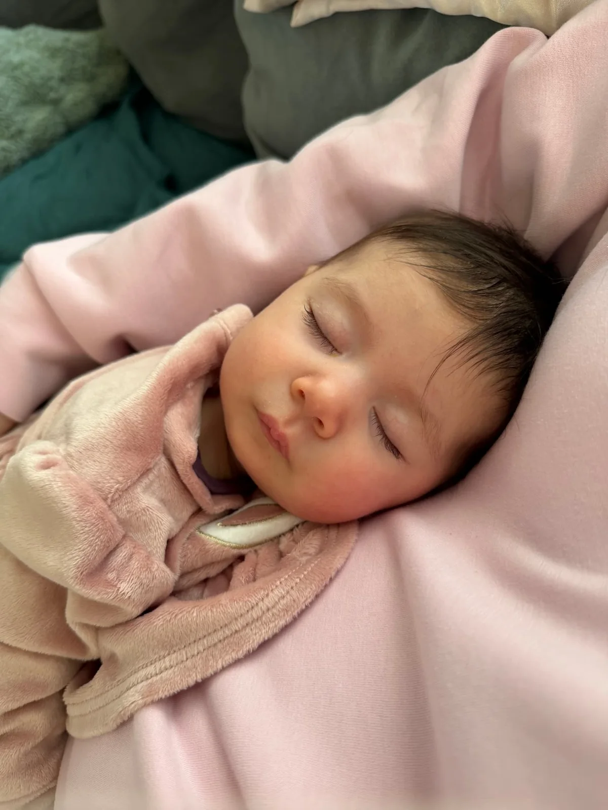 A baby asleep on soft pink blankets in warm daylight