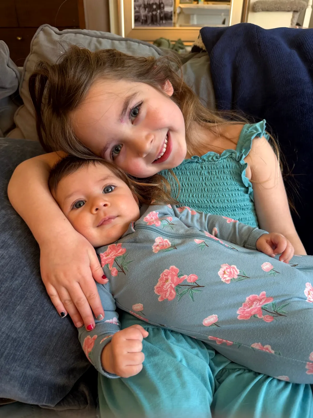 A big sister cuddling her baby sister on the couch